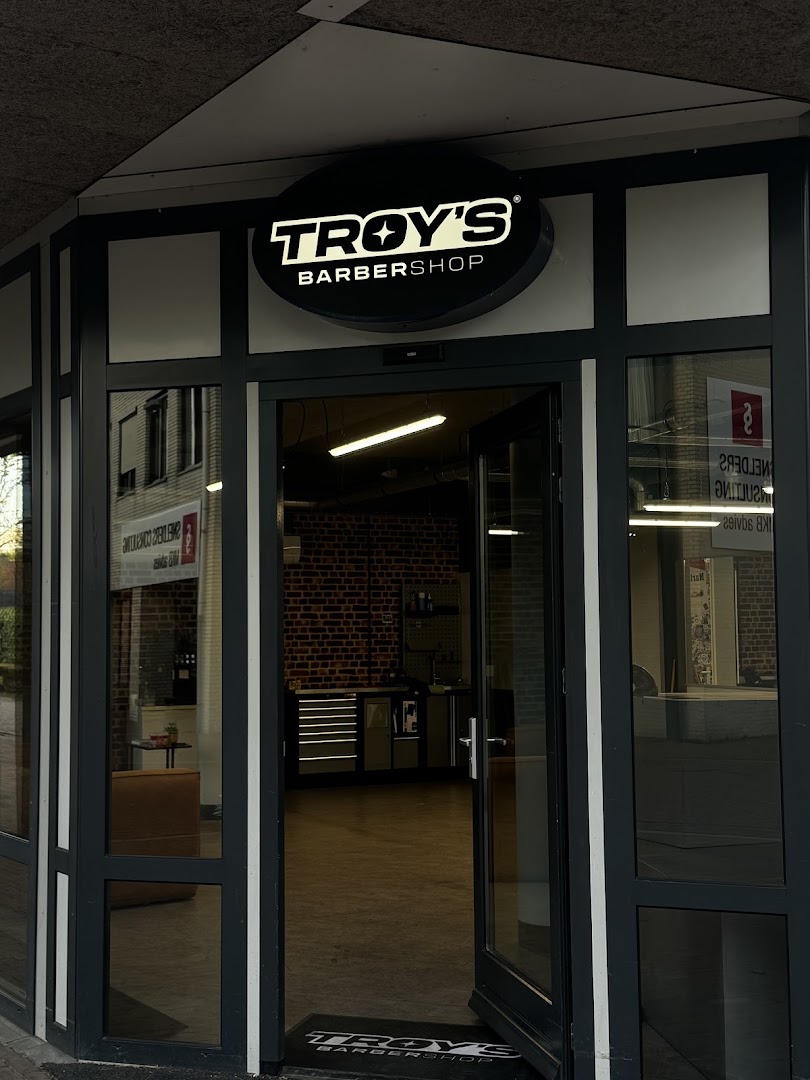 De ingang van Troy's Barbershop aan de Markt in Hapert, met het ronde TROY'S BARBERSHOP-uithangbord boven de deur